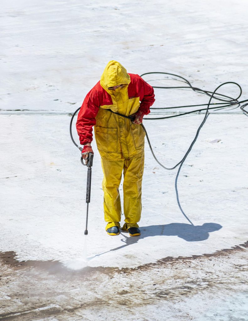 a man in a white coverall spray painting a roof